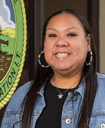 TCC Student Meredith Good Voice-Birdcreek poses in front of the Muscogee Nation Seal 