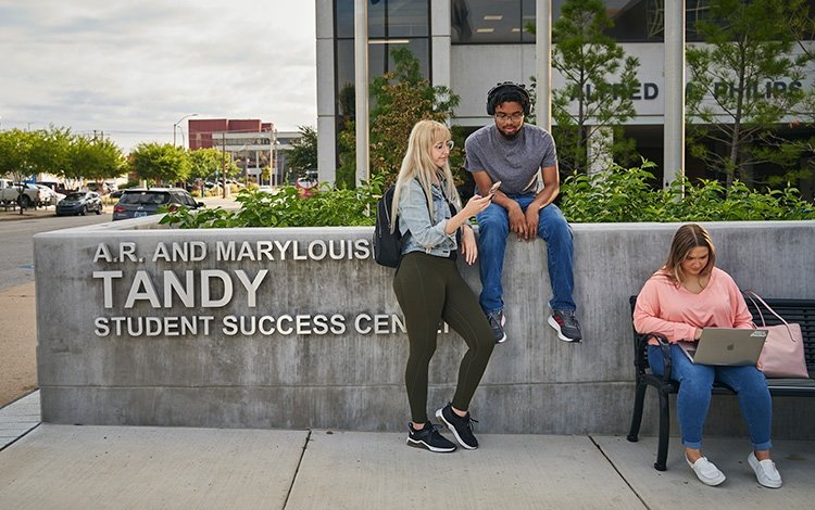 Three TCC Students stand and sit outside the A.R. and Marylouise Tandy Student Success Center